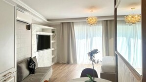 Uma sala de estar moderna com uma mesa de jantar redonda, duas cadeiras, um sofá e uma TV fixada na parede.