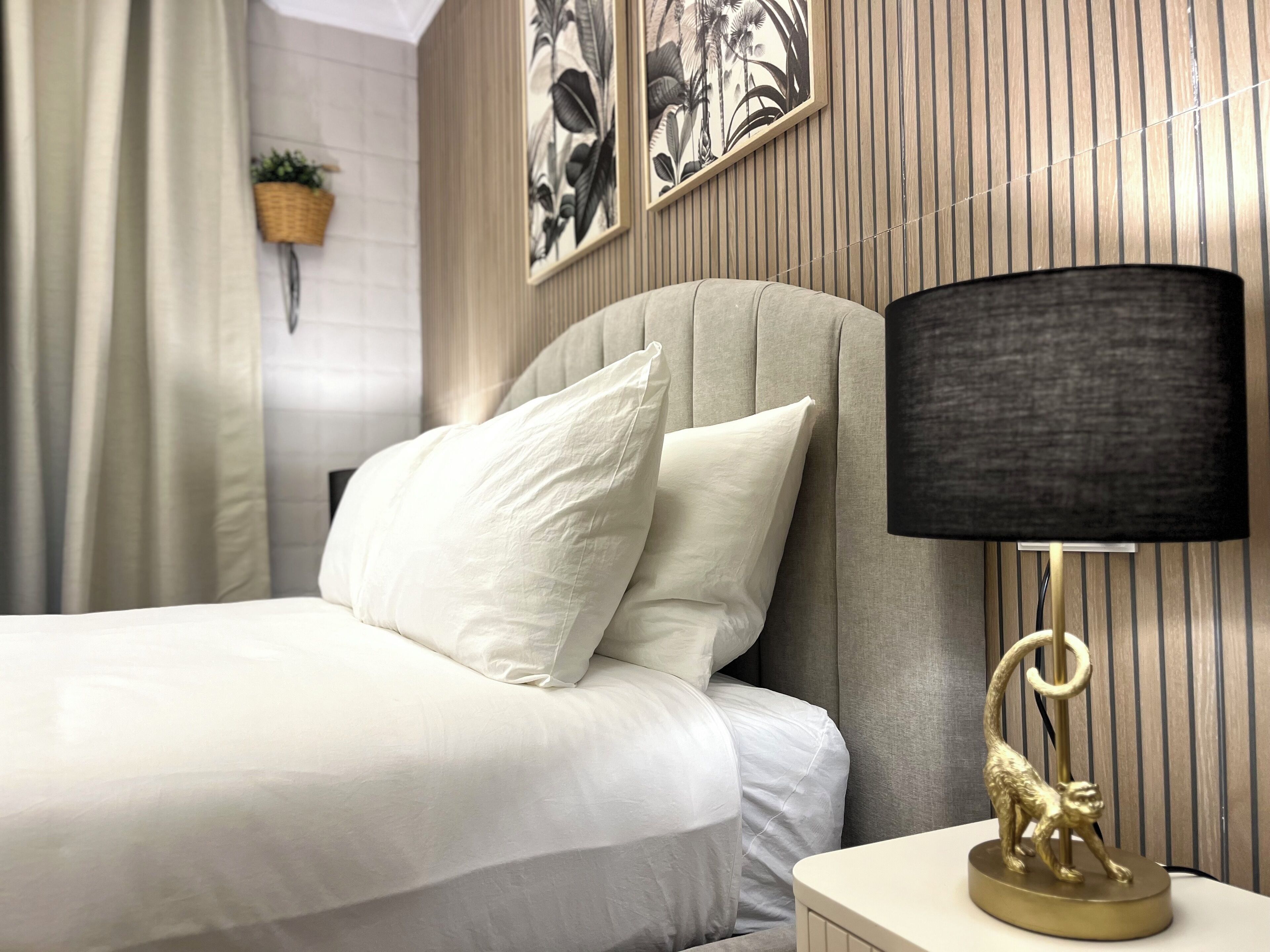 A neatly made bed with white linens and a gold lamp with a monkey base.