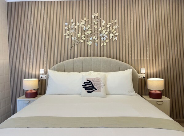 A neatly made bed with a white headboard, two bedside lamps, and a decorative wall piece above the bed. - Torri Studios (Sliema)