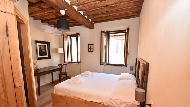 Ein Schlafzimmer mit einem hölzernen Bett, einem Schreibtisch und einem Stuhl. Es gibt ein Fenster mit Rollläden, ein Bild an der Wand und eine Lampe auf dem Nachttisch.