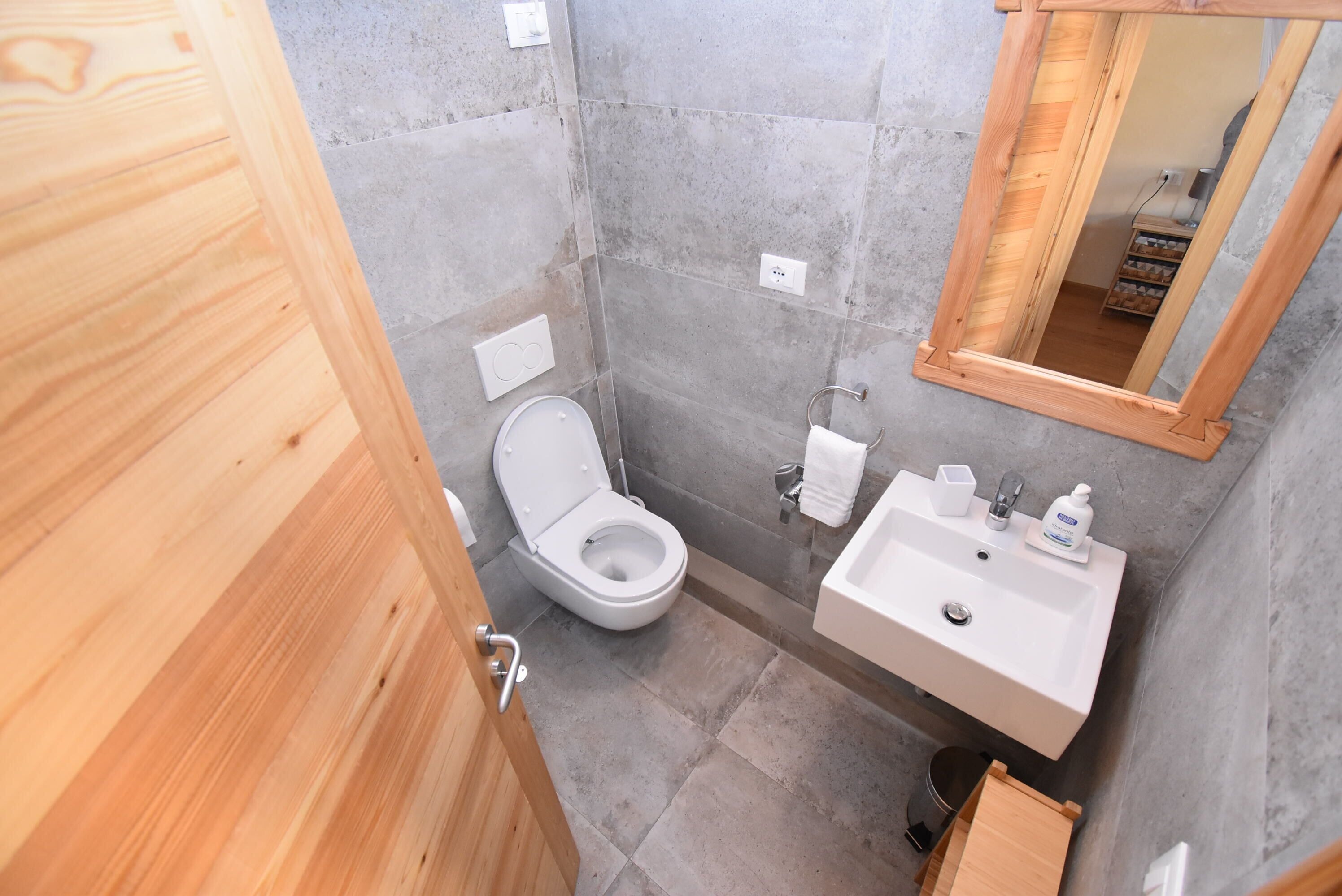 Un bagno compatto con porta in legno, un water, un lavandino con specchio e un piccolo ripiano con articoli da toilette.