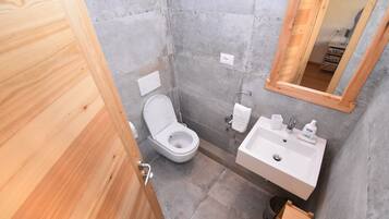 Un bagno compatto con porta in legno, un water, un lavandino con specchio e un piccolo ripiano con articoli da toilette.