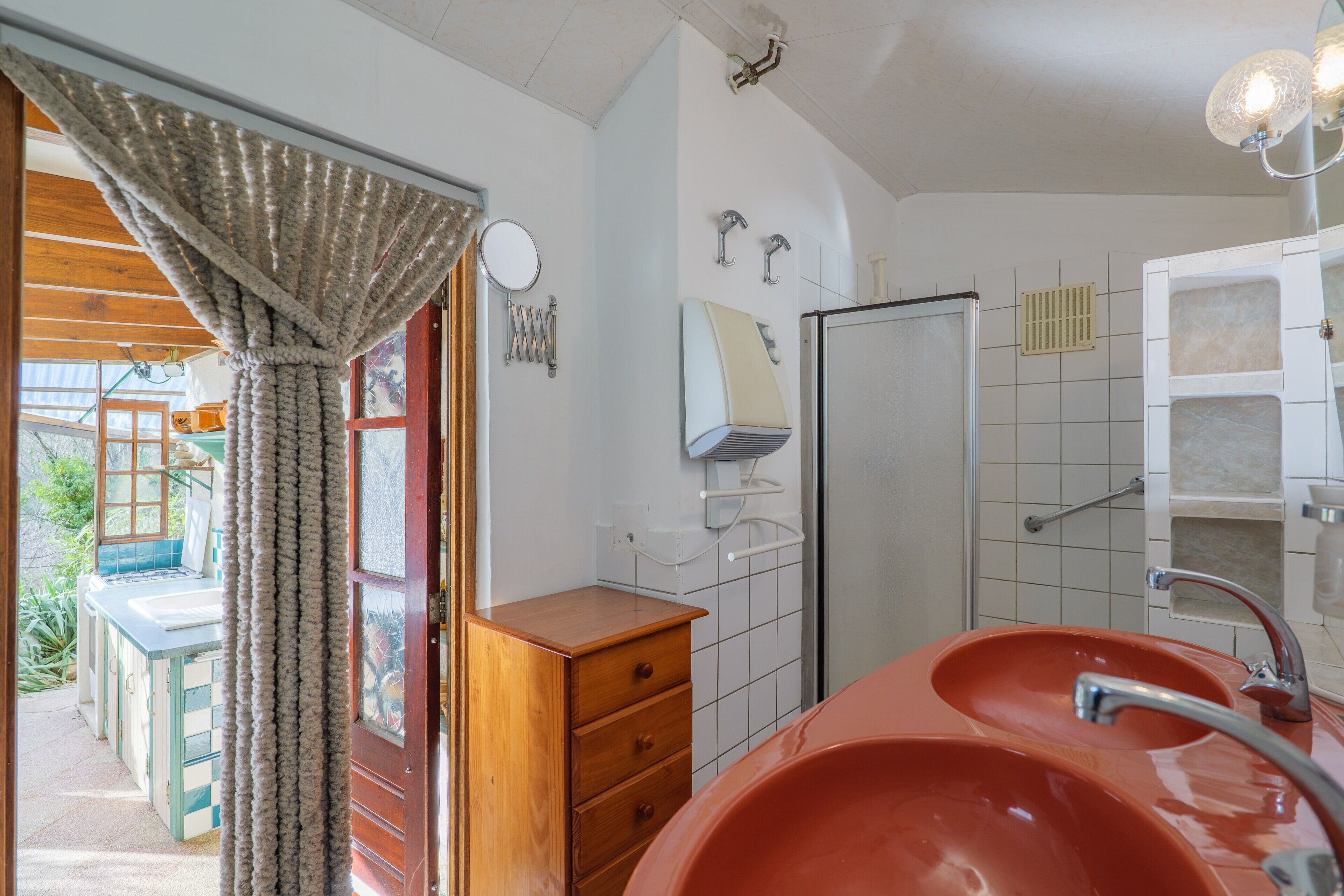 Ein Badezimmer mit einem großen, roten Waschbecken, einem Holzkabinet, einem Spiegel und einem Duschbereich.