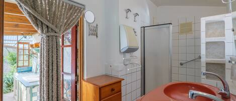 Ein Badezimmer mit einem großen, roten Waschbecken, einem Holzkabinet, einem Spiegel und einem Duschbereich.