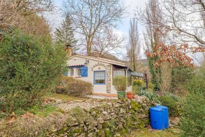 Uma casa rústica com parede de pedra, porta azul e um pequeno jardim com plantas em vasos.