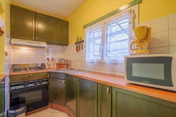Una cocina con gabinetes verdes, una estufa, un microondas y una ventana con cortinas de encaje.
