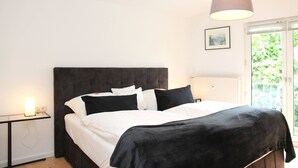 Une chambre à coucher avec un lit, une table de chevet, une lampe, une fenêtre et un tableau au mur.