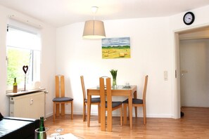 A dining area with a table, chairs, a hanging lamp, a painting, and a clock on the wall.