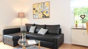 Un salon moderne avec un canapé en cuir noir, une table basse en verre, un tableau au mur, une lampe et une fenêtre donnant sur un paysage verdoyant.