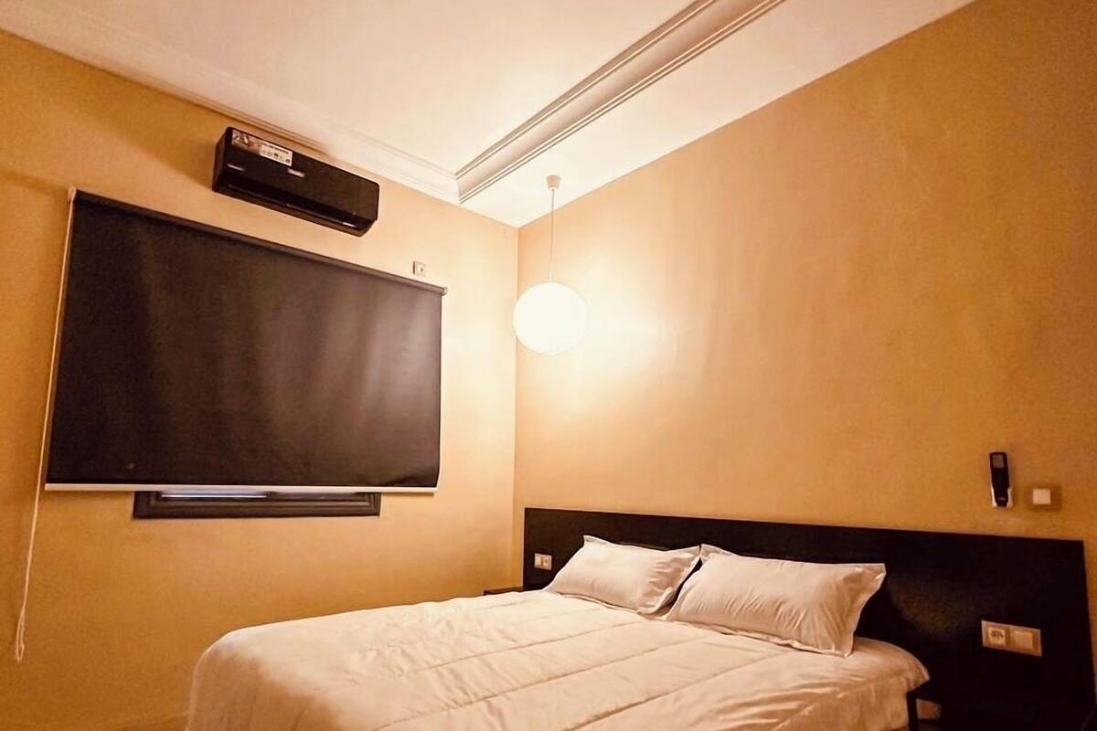 Een hotelkamer met een bed, een flatscreen televisie aan de muur, een nachtkastje en een wandlamp.