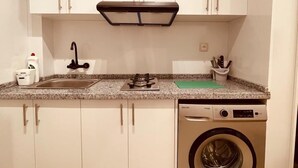 A compact kitchen with white cabinets, a built-in stove, a sink, and a front-loading washing machine. - Relax family Majestic (Ouarzazate)