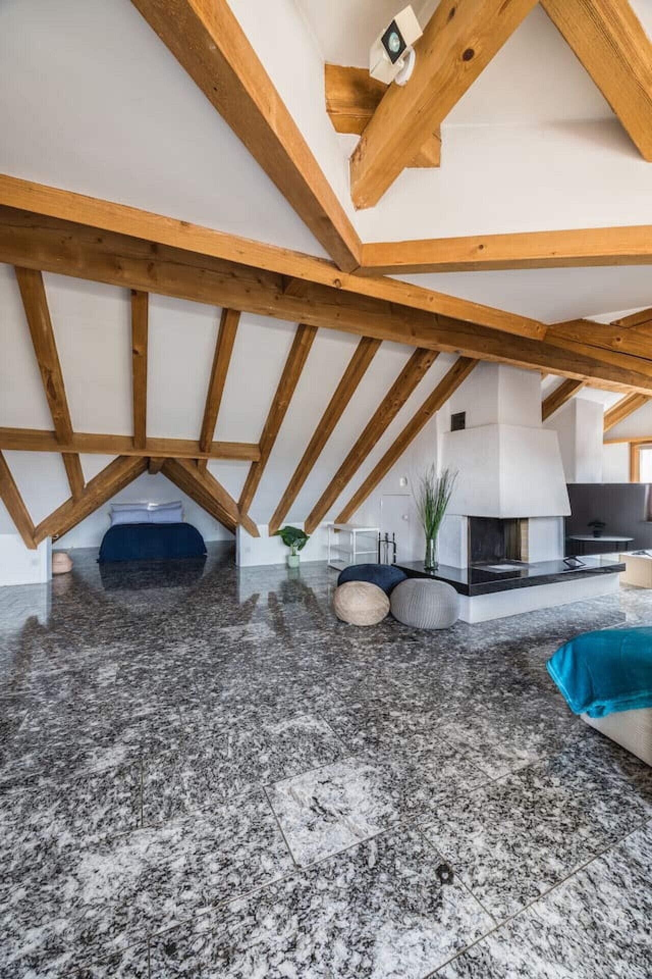 Een ruime loft met zichtbare houten balken, een open haard en een gepolijste stenen vloer.