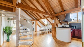 Een ruime loft met een houten trap, een eethoek en een keuken met rode kastjes.