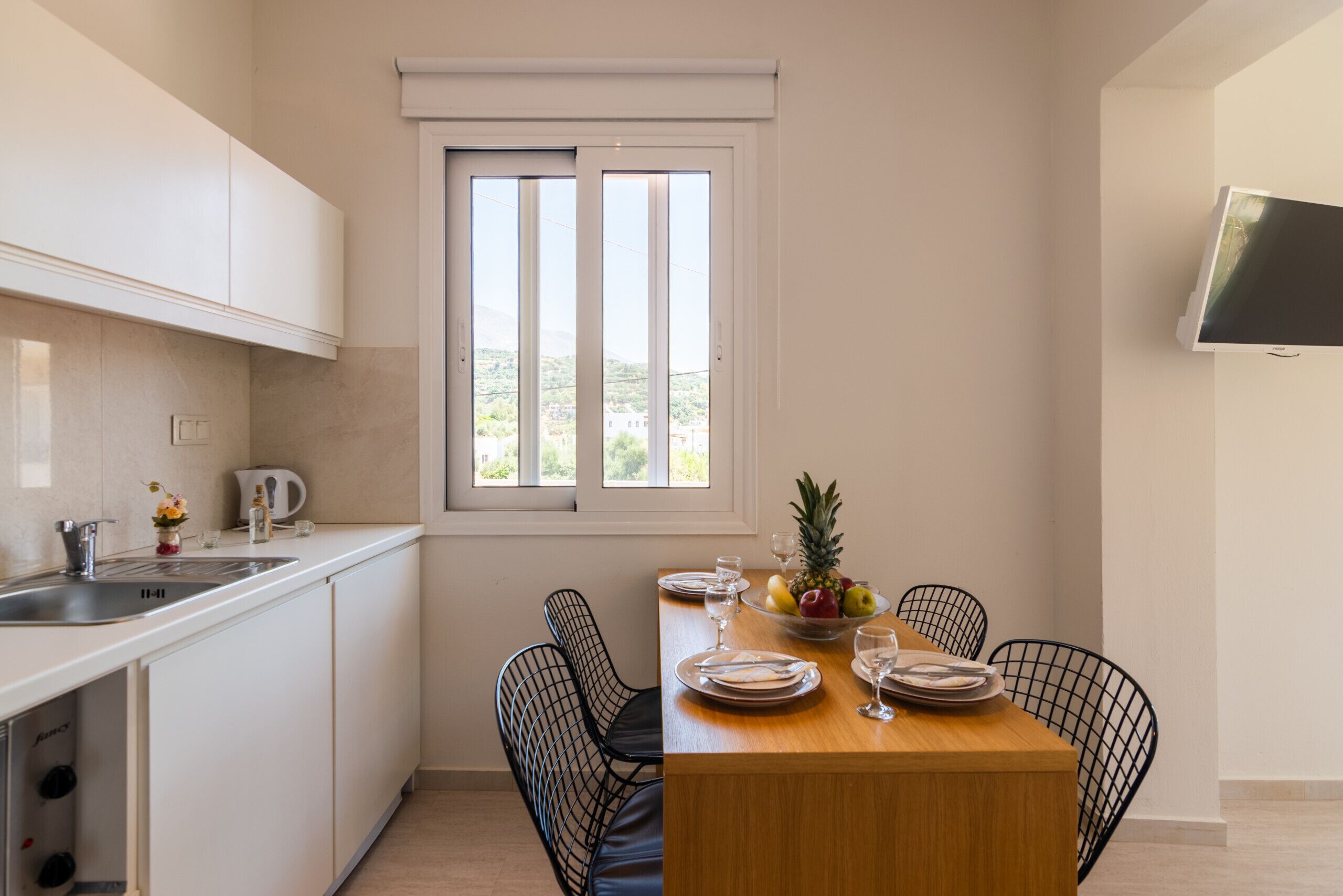 A compact kitchen with white cabinets, a wooden dining table, and black wire chairs.