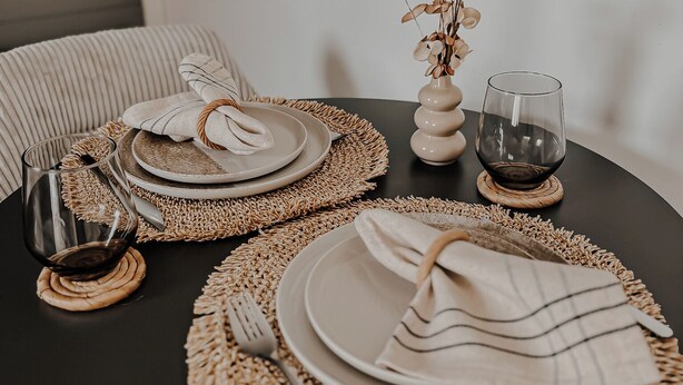 A round dining table set with plates, cutlery, and a glass of red wine on coasters.
