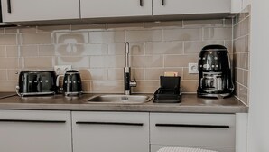 A modern kitchen with white cabinets, a tiled backsplash, and two coffee makers.