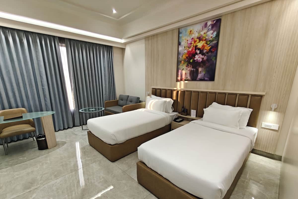 Una habitación de hotel con dos camas, un escritorio, una silla, una mesita y un cuadro en la pared.
