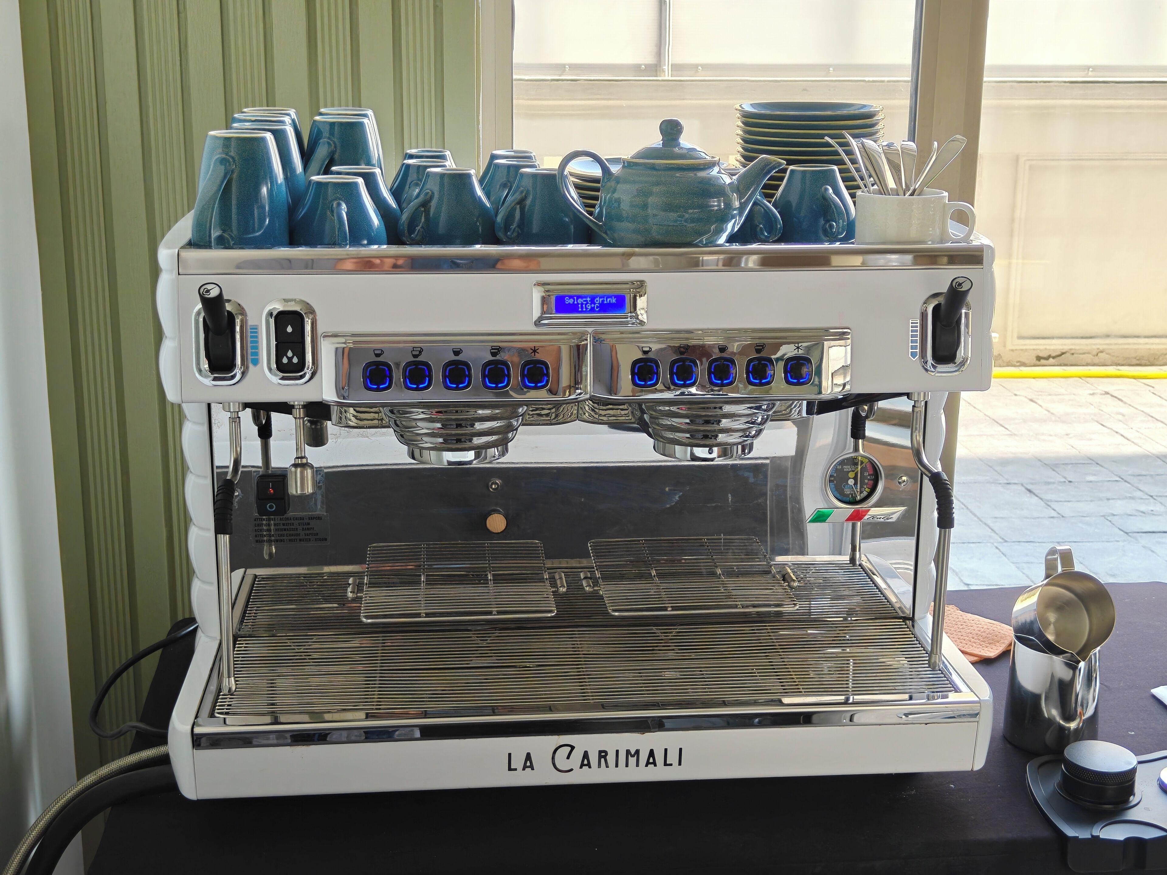 A La Carimali espresso machine with a digital display, multiple coffee cups, and a stack of plates.