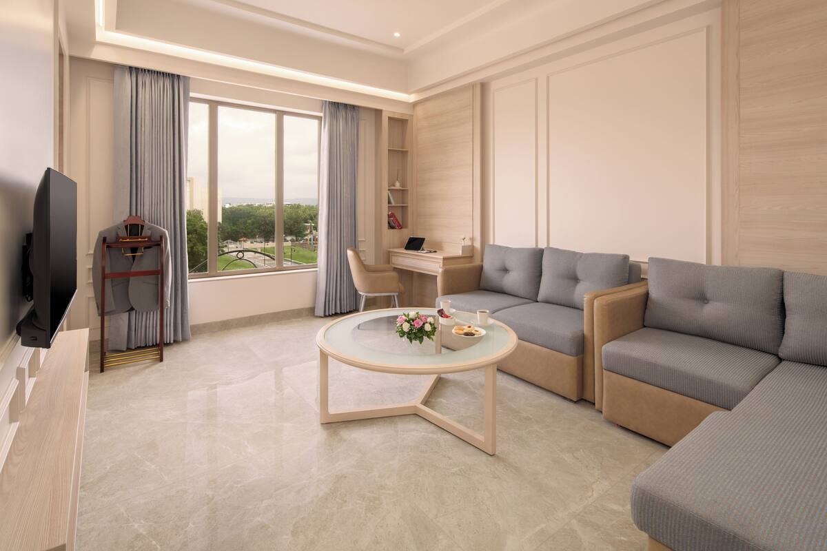 Una sala de estar moderna con sofá, una mesa de centro, televisor y vistas al exterior.