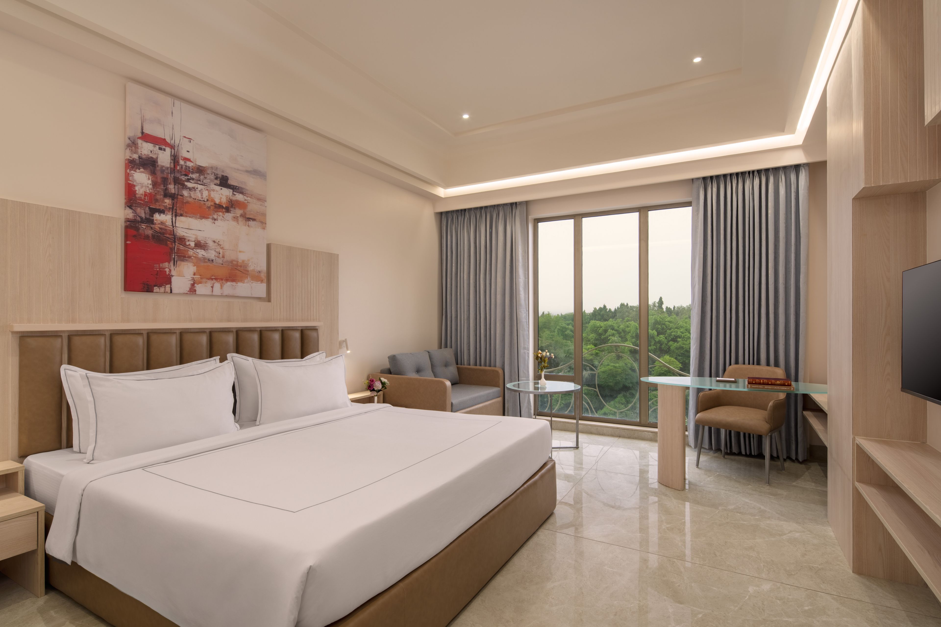 Habitación de hotel moderna con una cama grande, un escritorio, una silla, un televisor y un amplio ventanal con cortinas.