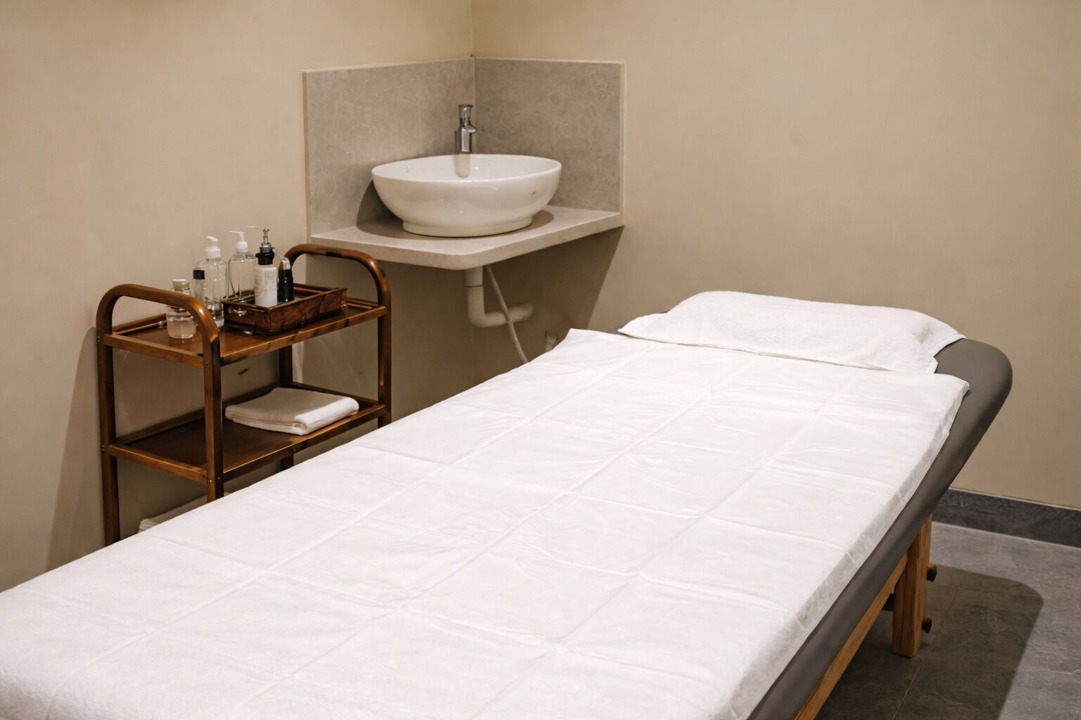 A single bed with a white mattress and a wooden bedside table with toiletries.