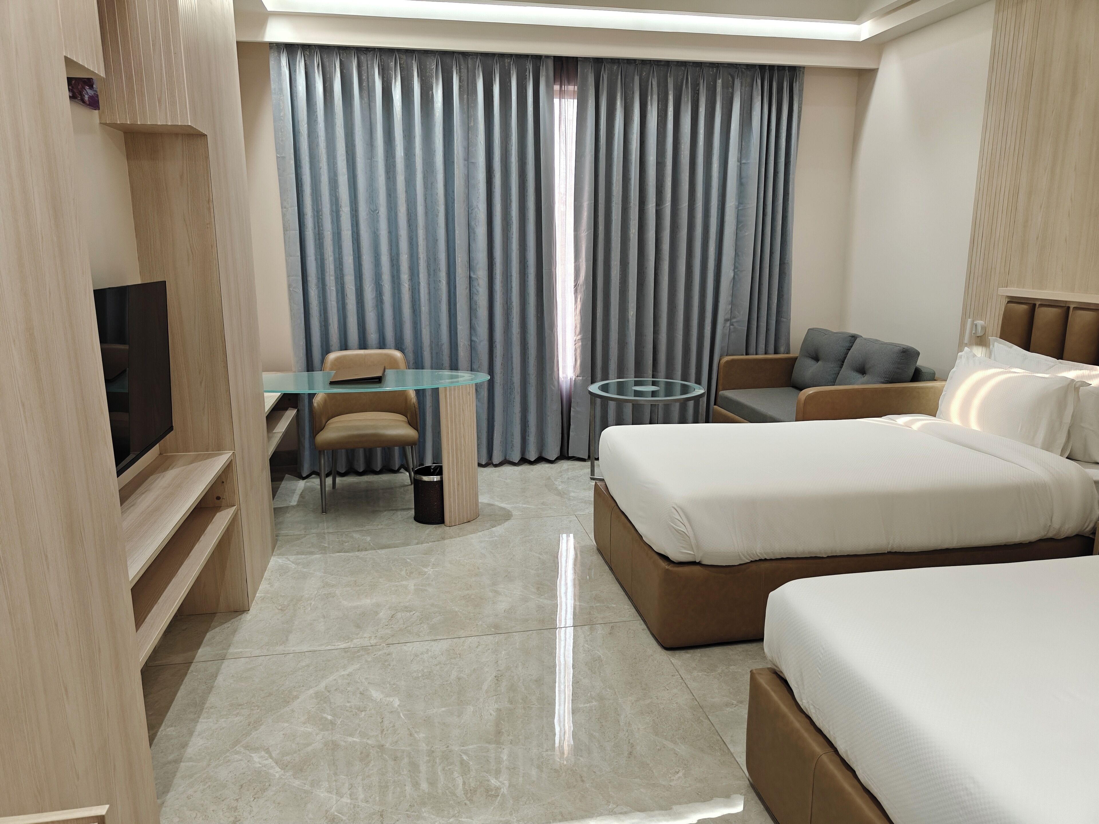 A hotel room with a bed, a desk, a chair, a TV, and a window with curtains.