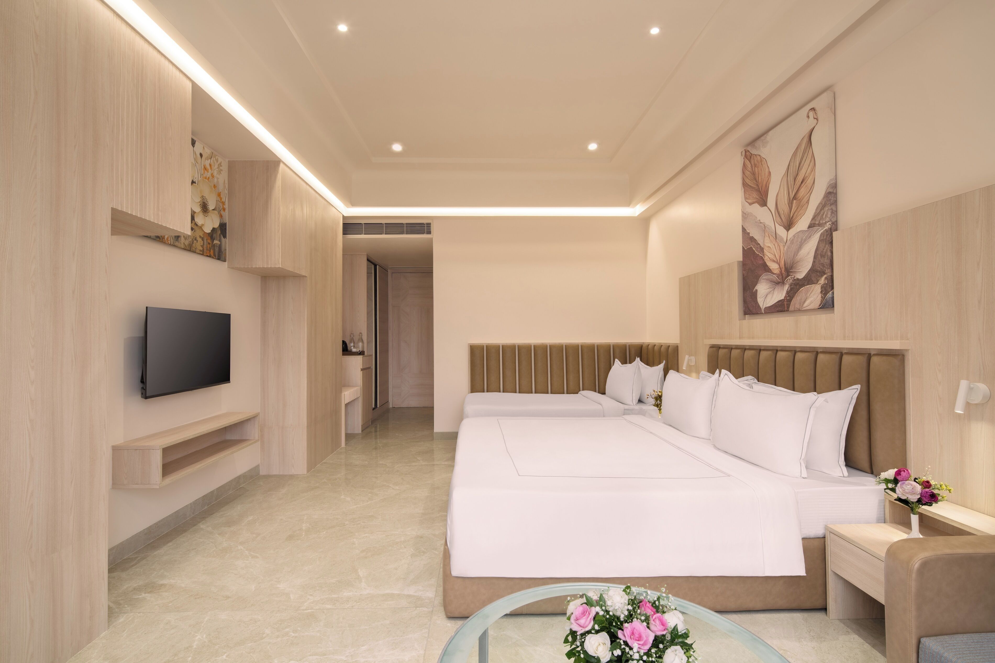 Habitación de hotel moderna con una cama grande, un televisor de pantalla plana, una mesita de noche con un florero y un estante fijado a la pared.