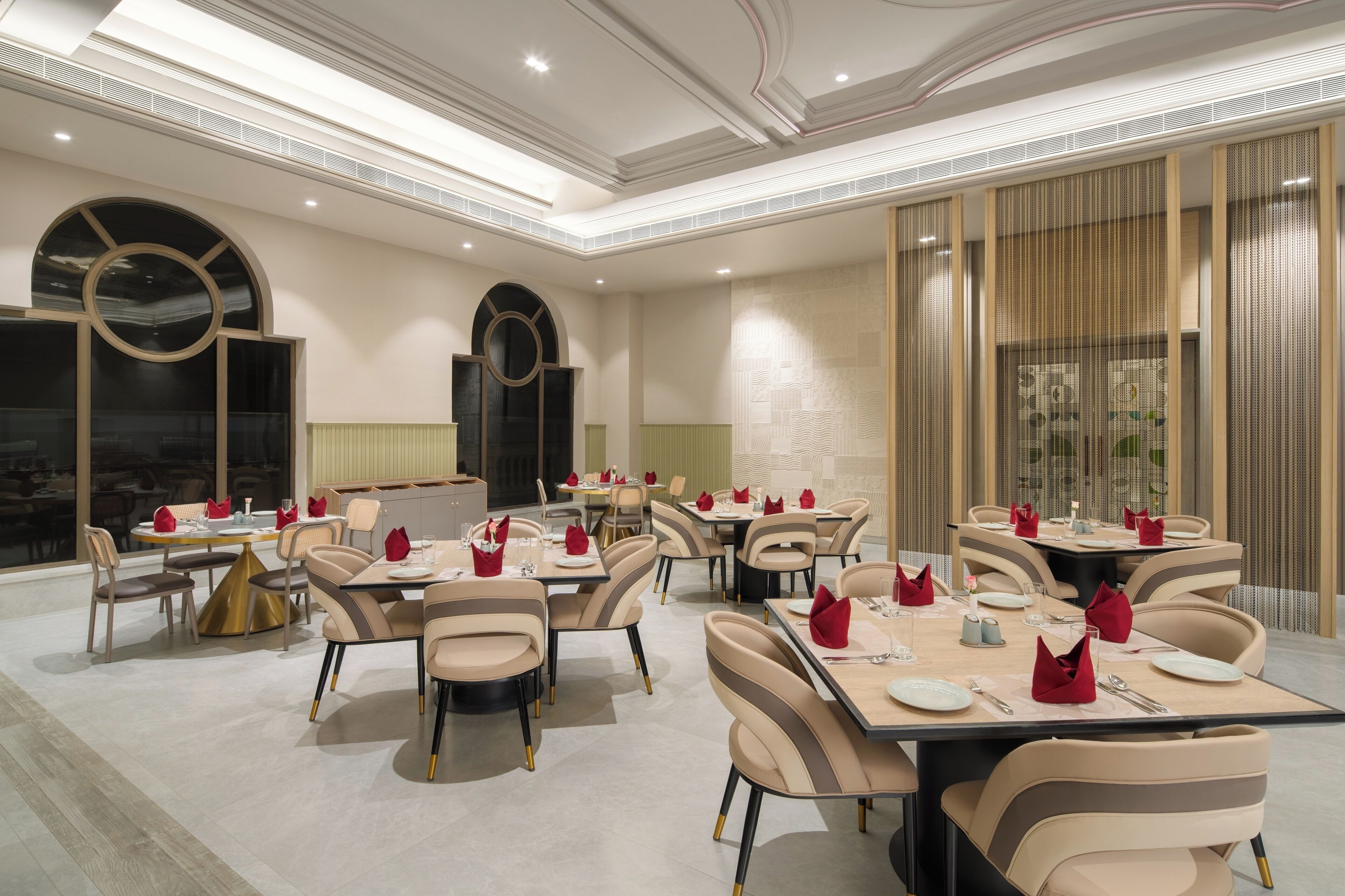 A spacious dining area with multiple tables and chairs, featuring a modern design with neutral tones and gold accents.