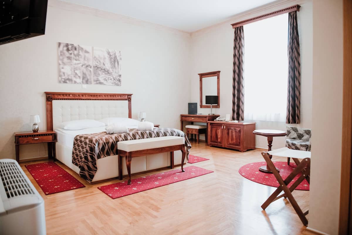 Una habitación de hotel con cama, mesita de noche, escritorio, silla y un amplio ventanal con cortinas.