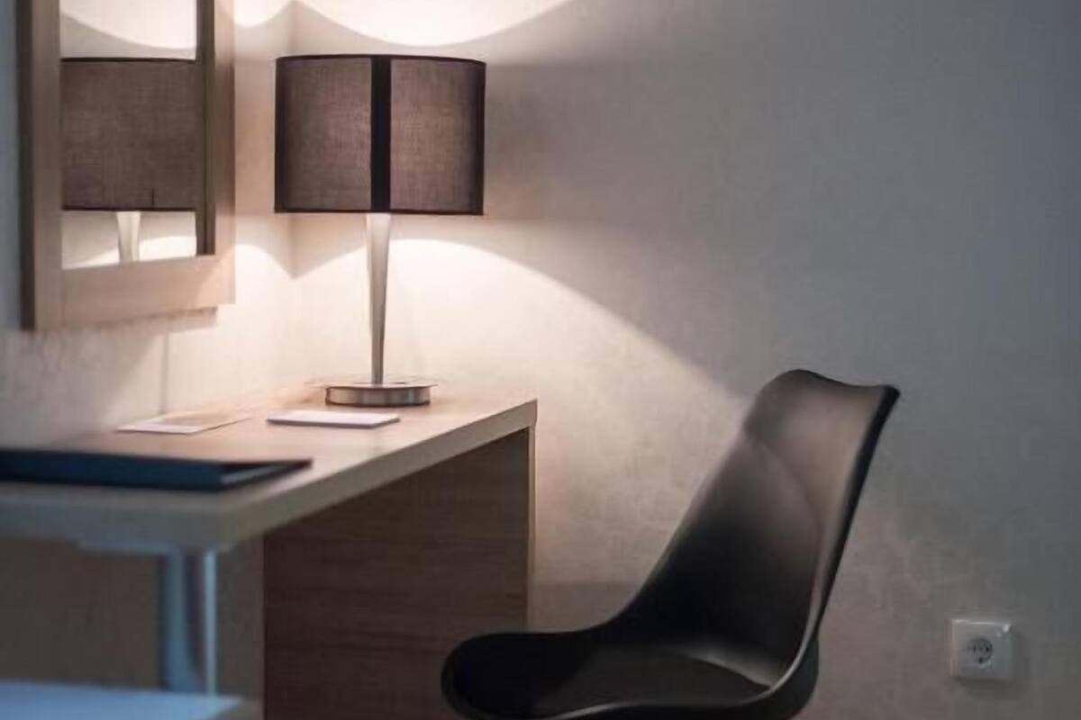 Una habitación moderna con escritorio, silla, lámpara y espejo en la pared.