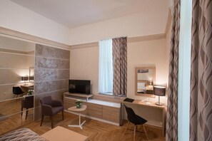 A modern hotel room with a wooden floor, a flat-screen TV, a desk with a lamp, a chair, and a small table with a plant. - Hotel Kurija Janković (Lukač)