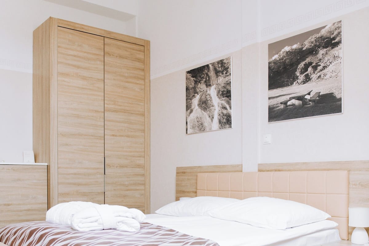 Un dormitorio moderno con un armario de madera, una cama con ropa de cama estampada, una mesita de noche con una lámpara y dos fotografías blanco y negro en la pared.