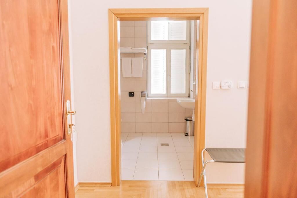 A hallway leading to a bathroom with a window, a sink, and a trash bin.