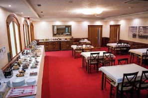 Un espace repas avec des tables et des chaises, un buffet proposant divers plats, et un miroir accroché au mur.