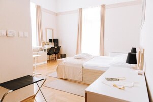 Habitación de hotel con cama, mesita de noche, silla, escritorio y una pequeña mesa con lámpara.