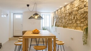 Un espace de salle à manger moderne avec une table en bois, six chaises, un luminaire suspendu noir et un mur en pierre.
