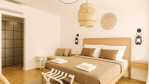 Une chambre bien rangée, avec un grand lit, des tables de chevet, une chaise et un luminaire suspendu.