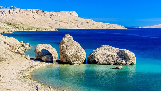 Une plage avec de gros rochers dans l’eau et un ciel bleu dégagé.
