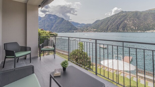 Uma varanda com vista para um lago e montanhas, equipada com cadeiras e uma mesa.
