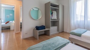 Um quarto com cama, escrivaninha, guarda-roupa e espelho.