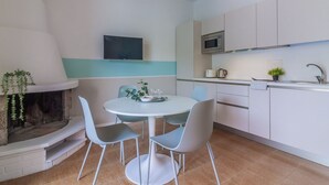 Cozinha moderna com armários brancos, micro-ondas e forno embutido. Há uma área de jantar com uma mesa redonda e quatro cadeiras.