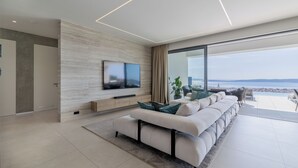 Ein modernes Wohnzimmer mit großem Flachbildfernseher, einer Couch und Blick auf das Meer.