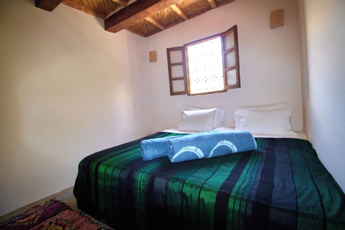 A bedroom with a bed, a window, and a wooden ceiling.
