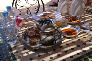 Una mesa con un juego de té, tazas y diversas comidas, incluyendo aceitunas y un recipiente con miel.