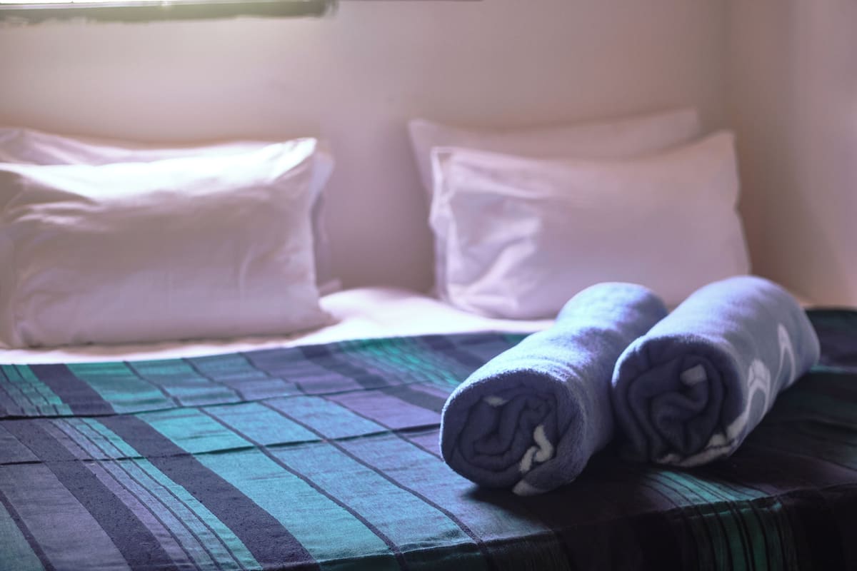 A bed with a green and blue checkered bedspread, two rolled towels, and white pillows.