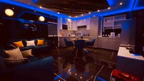Ein modernes Wohnzimmer mit schwarzem Fliesenboden, einem blauen Sofa mit Kissen und einem Essbereich mit Stühlen.