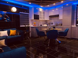 A modern kitchen with a dining area, featuring a blue sofa, a round table, and blue chairs. - AzureGold Apartment (Senglea)