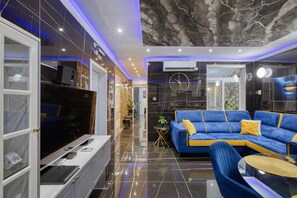 A modern living room with a blue sofa, a flat-screen TV, and a marble floor. - AzureGold Apartment (Senglea)