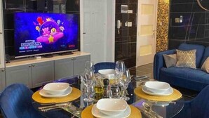 Ein moderner Essbereich mit einem runden Tisch, blauen Stühlen und einem Fernseher, der die Sendung 'Baby Shark's Space Adventure' zeigt.