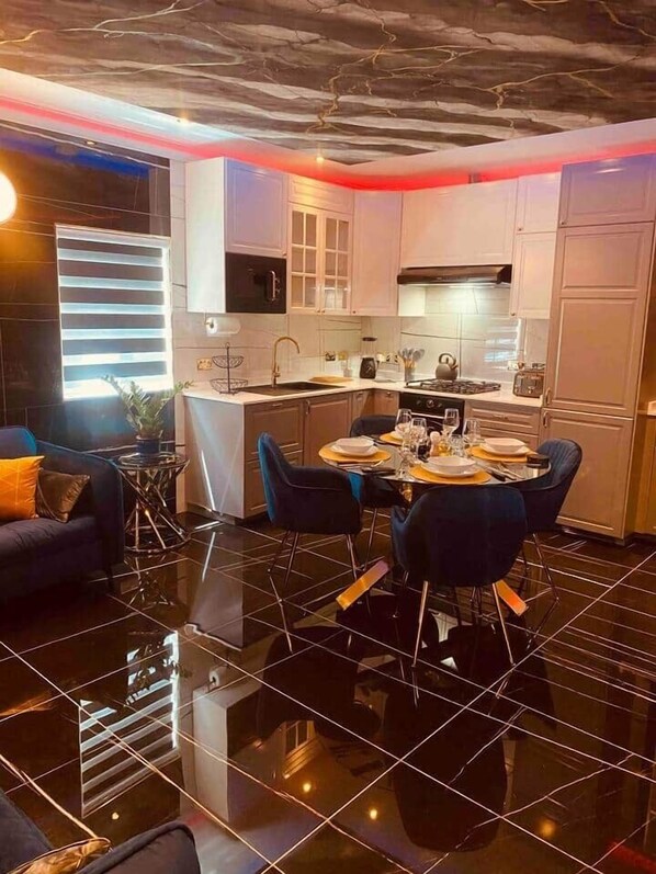 Une cuisine moderne avec un coin repas, dotée d’un sol carrelé noir, de meubles blancs et d’un îlot central.